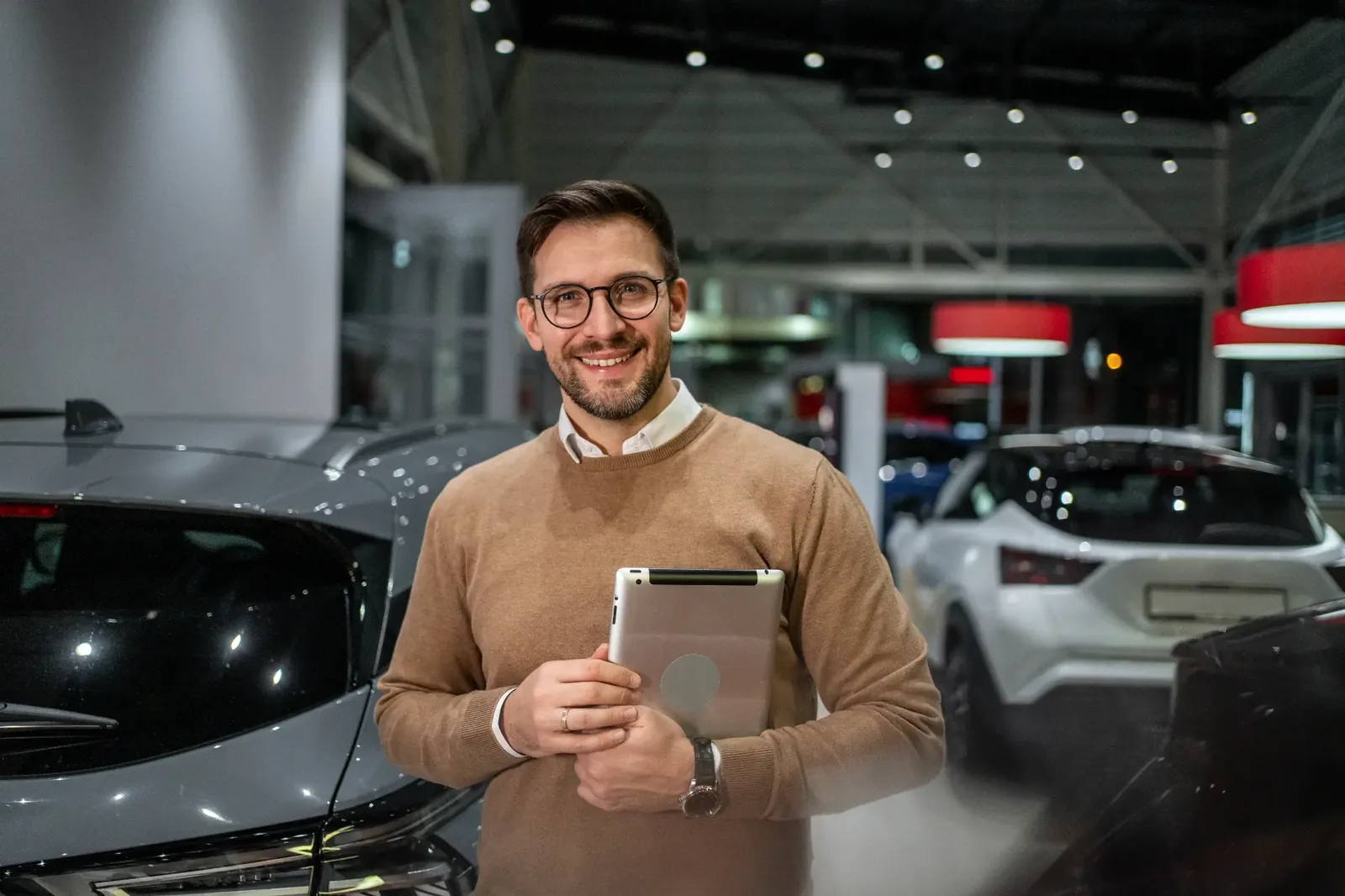 Asesor de una concesionaria sonriente con una tablet junto a los autos del showroom