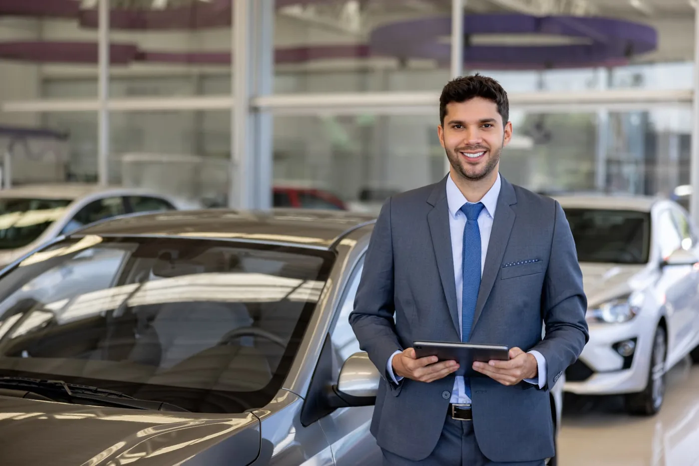 Asesor comercial sonriente con una tablet junto a los autos del showroom de la concesionaria